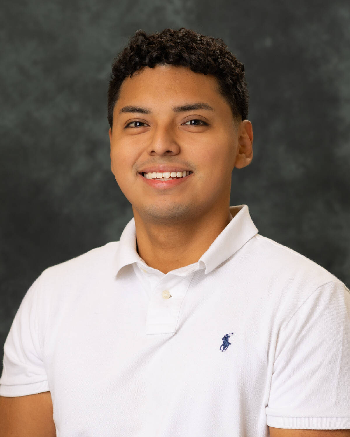 Student wearing a white polo shirt posing for a studio headshot